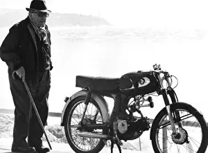 Old man standing next to a motorcycle near a beach