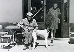 Shirley Prints: An older man with his pet dog seated at a small table on a terrace outside a cafe or restaurant in the south of France