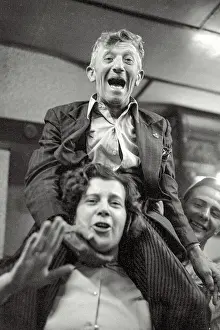 Antwerp Prints: Older slight man sitting on shoulders of younger woman during dancing to small band playing in daylight at local bar