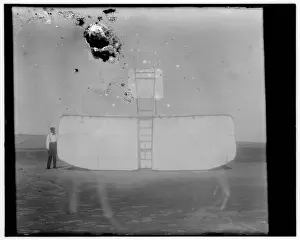 Orville at left wing end of upended glider, bottom view; Kit
