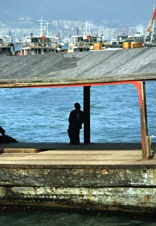 Images Dated 8th August 2019: Silhouette of man sat on a bollard on a pier in Hong Kong