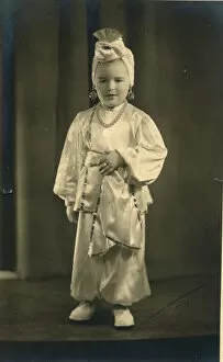 A small boy (or girl) dressed in a turban and harem pants in an Arabian Nights style