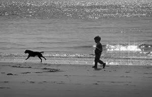 Leaping Gallery: Small boy walks with dog along the tideline - Tenby Beach
