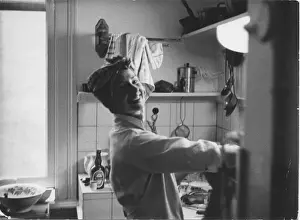 A smiling young woman in a headscarf and apron washing up or preparing food in a kitchen