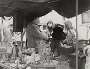 An stall holder chats up two young women at Portobello Road antiques market, London. Date: late 1960s