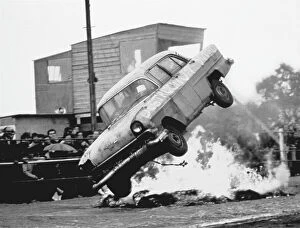 Destruction Collection: A stunt car flies through the air over a bonfire of tyres, watched by spectators standing in
