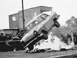 Stunts Collection: A stunt car flies through the air over a bonfire of tyres, watched by spectators standing in