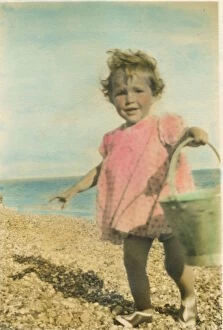 A toddler on the beach at Bognor Regis with a bucket in hand. Date: 1920s