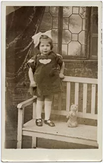 Enormous Collection: TOY CAT, a little girl with an enormous bow in her hair stands on a garden bench with her
