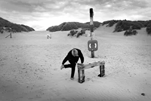 Woman bends over to brush sand from her feet, Harlech beach Woman bends over to brush sand from her feet, Harlech beach