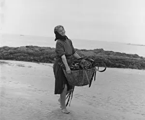Woman carrying basket of seaweed along a beach