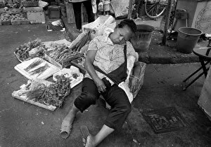 Exhausted Collection: A woman sleeps at her vegetable stall in a Hong Kong market
