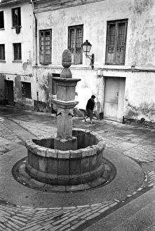 Cantabria Prints: A woman walks past an old stone drinking water fountain