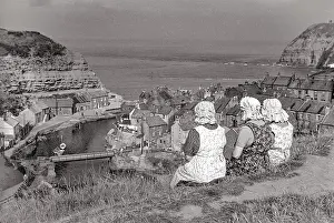 Three women in bonnets and pinifores looking down on Staithes harbour Date: 1947 - 1948