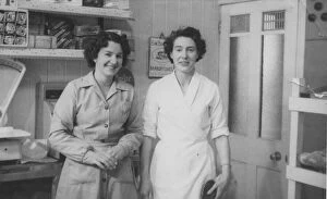 Two women pose for their photograph in a bakers shop. Date: c.1953