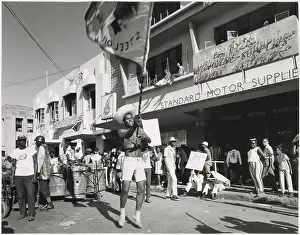 Afro Prints: A young man in shorts dances and waves a flag about at the Port of Spain Carnival