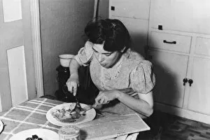 News Paper Gallery: Young woman in a kitchen eating a plate of food