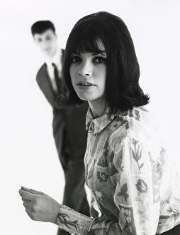 Blouse Collection: A young woman poses in the foreground with an out of focus male standing behind. Date: mid 1960s